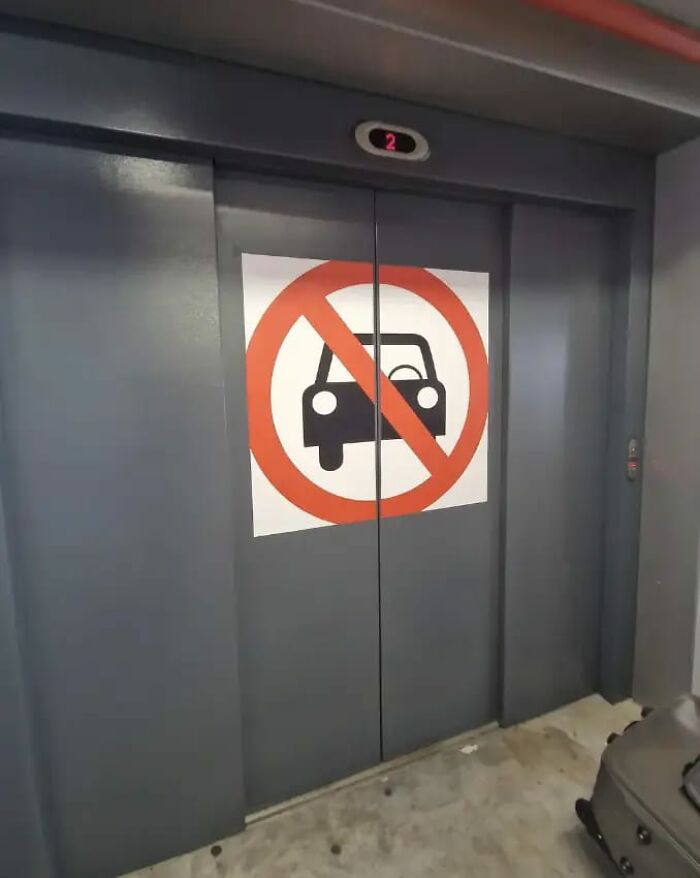 Ascensor con cartel divertido de aviso legal de prohibición de coches para evitar demandas legales.