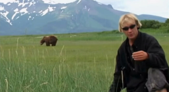 Hombre en campo con oso al fondo, foto inquietante en apariencia normal.