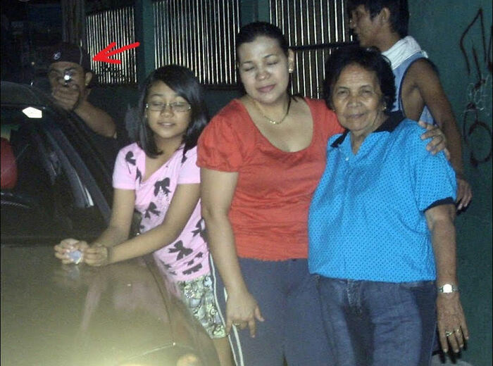 Un grupo posando para una foto nocturna, mientras una figura inquietante aparece al fondo.