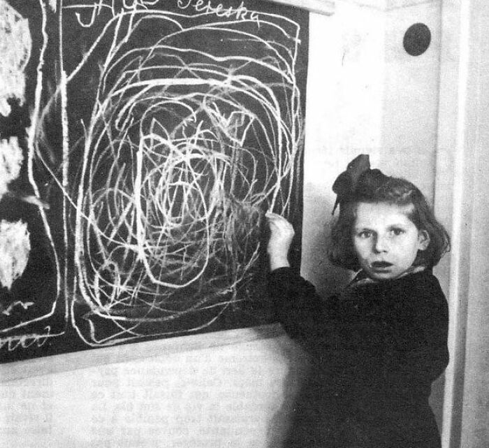 Niña dibujando en pizarra con trazos desordenados, creando una escena inquietante.