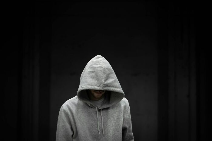 Persona con sudadera gris con capucha baja, destacando una atmósfera de paranoia y terror en fondo oscuro.
