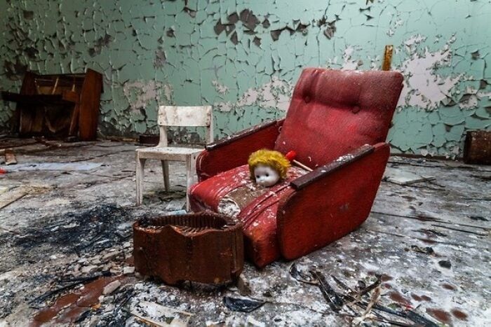 Muñeca en silla roja en habitación deteriorada, símbolo de fotos inquietantes con historia oculta.