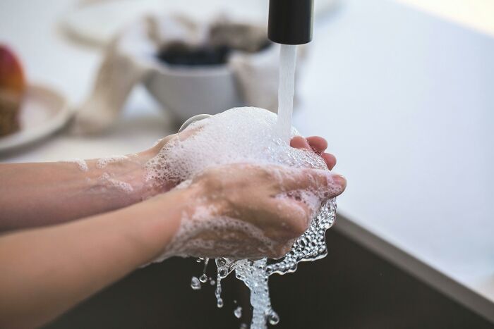Persona lavándose las manos con jabón bajo el agua corriente en un fregadero.
