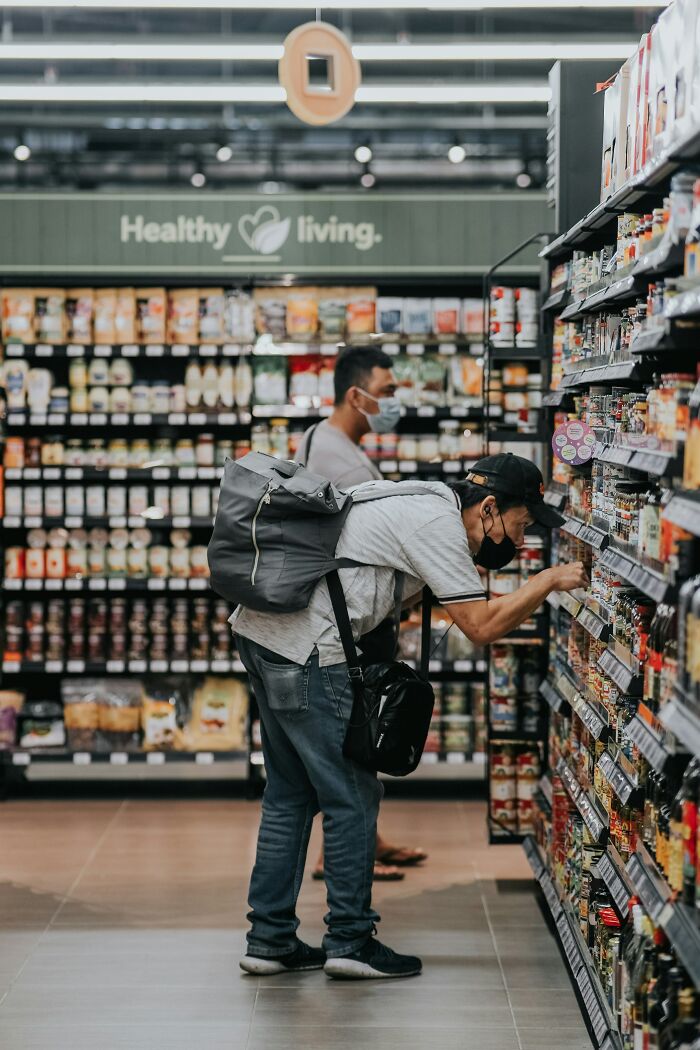 Hombres comprando en supermercado, uno con mochila y ambos usando mascarillas.