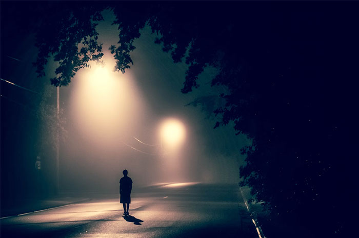 Hombre solitario caminando por una calle iluminada con farolas en la noche.