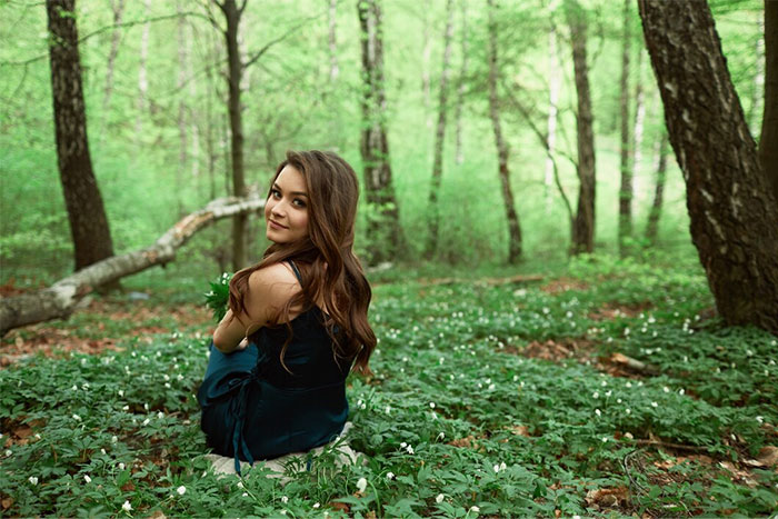 Mujer en bosque primaveral, sentada en el césped, mirando hacia la cámara.
