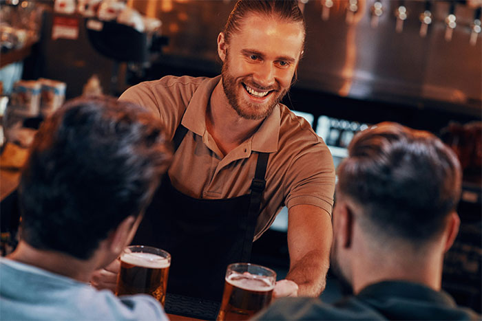 Barman sirviendo cervezas a dos clientes en un bar, todos sonriendo. Coincidencias increíbles que parecen falsas.