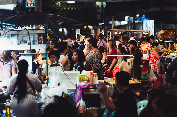 Multitud en un mercado nocturno bullicioso con puestos iluminados y varias personas, una coincidencia asombrosa de diversidad.