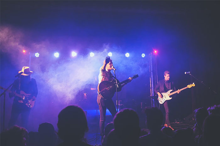 Banda en concierto en un escenario iluminado con efectos de humo, creando coincidencias visuales sorprendentes.