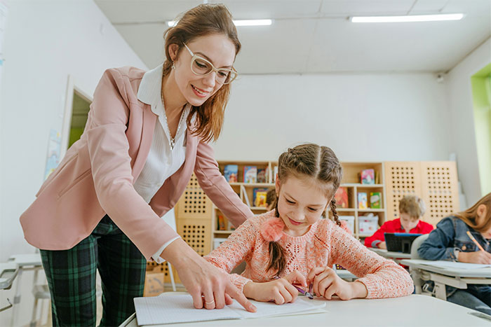 Maestra enseñando a una niña en clase; coincidencia sorprendente en educación.