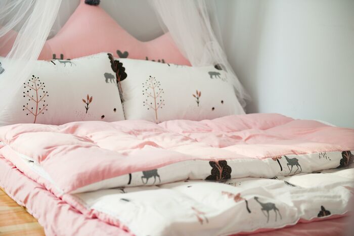 Cama con edredón rosado y almohadas estampadas, típico en hogares de clase media.