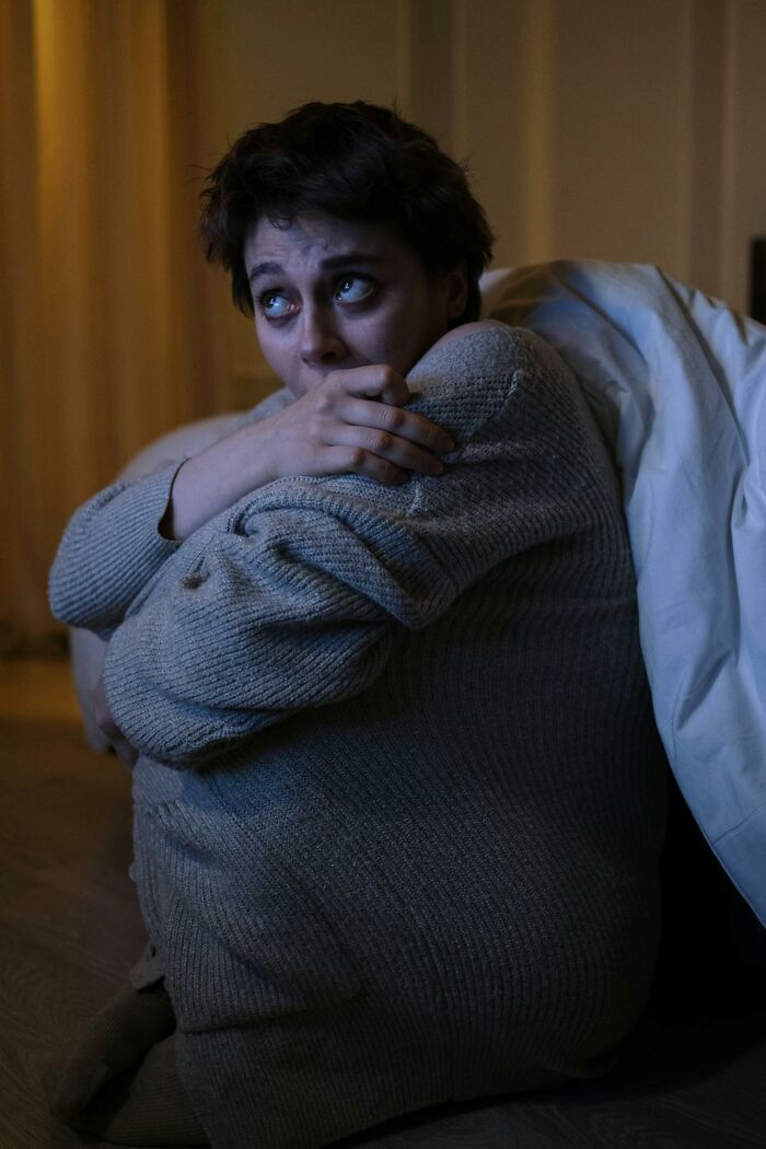 Persona asustada envuelta en una manta, reflejando terror real en su expresión, sentada en un entorno oscuro.