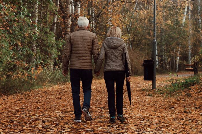 Pareja mayor caminando por sendero otoñal, enfrentando miedo real en bosque.