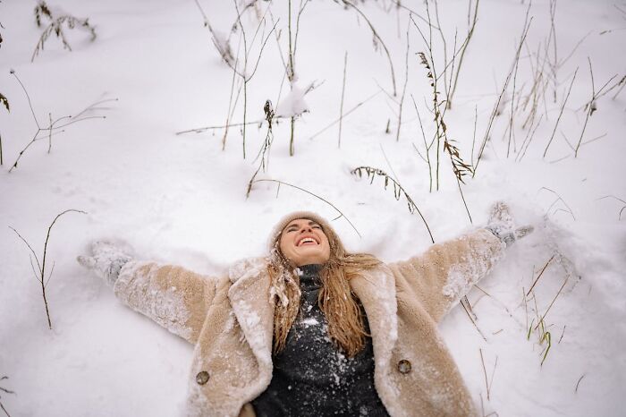 Persona disfrutando en la nieve, sonriendo mientras yace con los brazos extendidos, rodeada de copos de nieve.