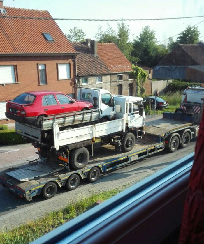 Transporte inusual de un camión y un coche rojo, apilados sobre un remolque en una calle residencial.