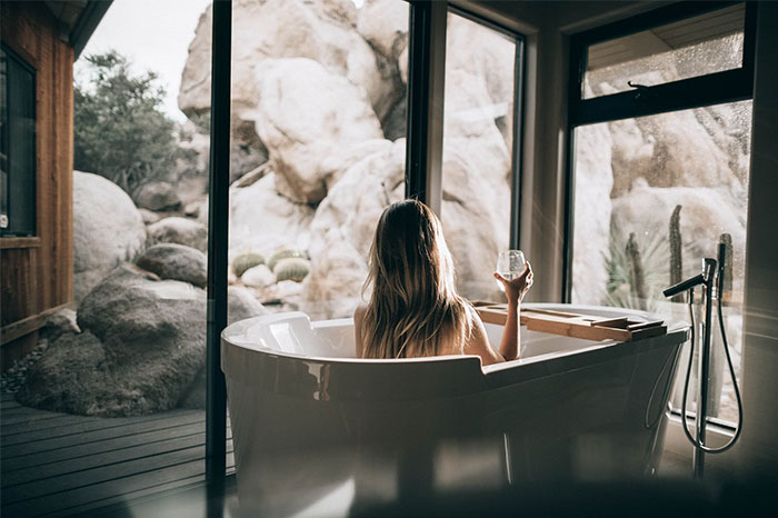 Una mujer sentada en una bañera, sosteniendo una copa de vino, disfrutando de una vista al jardín.