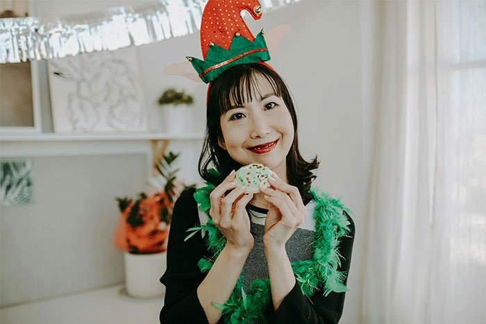 Persona con gorro festivo y plumas verdes, sujetando una galleta decorada, reflejando errores comunes en redes sociales.