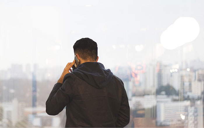Hombre de espaldas hablando por teléfono frente a una ventana con vista a la ciudad.