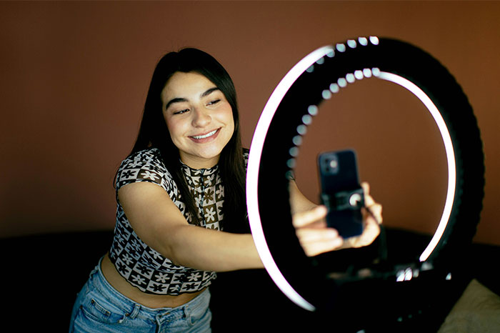 Persona sonriendo mientras se toma una selfie con anillo de luz, ilustrando fallos al publicar en redes sociales.