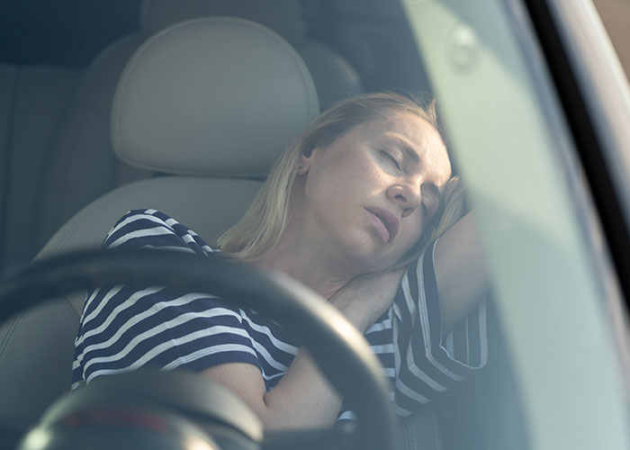 Mujer rubia con camisa de rayas durmiendo en un coche.