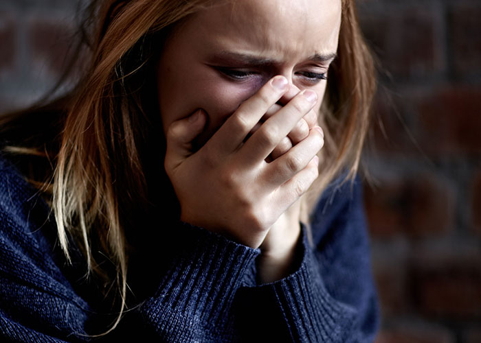 Persona llorando, cubriendo su rostro con las manos, en un momento de descubrimiento de odio por parte de sus amigos.