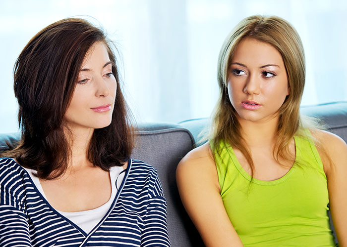 Dos mujeres sentadas en el sofá, mirándose con desconfianza, representando tensiones entre amigos.