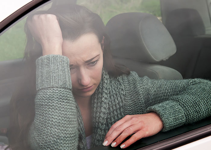 Mujer pensativa en un coche, con suéter verde, mirando preocupada. Sentimientos de odio por sus amigos.
