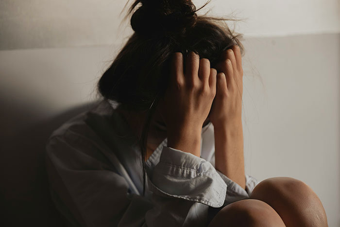 Persona sentada, cabizbaja, con las manos en la cabeza, simbolizando el trauma emocional.