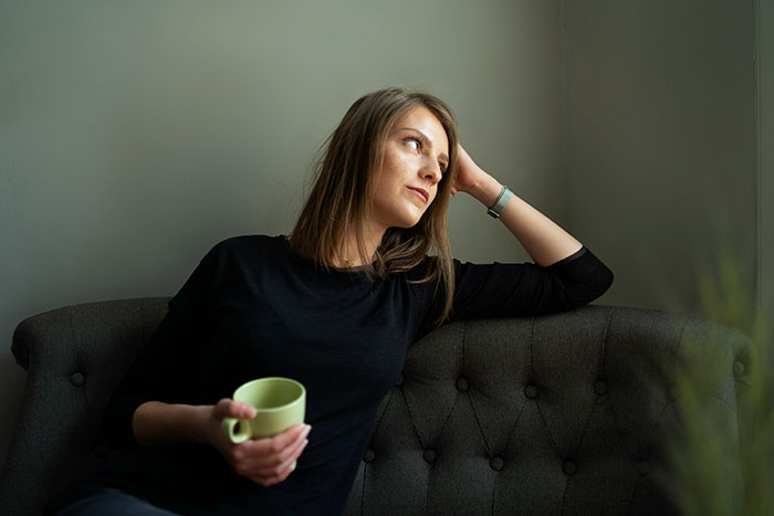 Mujer pensativa con taza verde, reflejando señales de traumas pasados, sentada en un sofá oscuro.