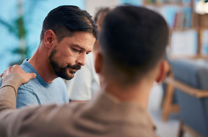 Hombre reflexionando, recibiendo apoyo emocional de otra persona, simbolizando signos de trauma pasado.