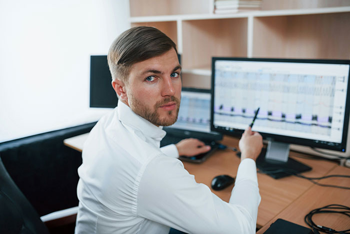 Hombre en oficina señalando pantalla de computadora con gráficos, posible análisis de señales de traumas.