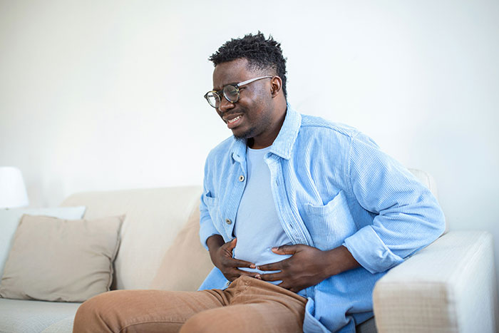 Hombre con dolor abdominal en sofá, ilustrando personas que aun siguen vivas por decisiones espontáneas importantes.