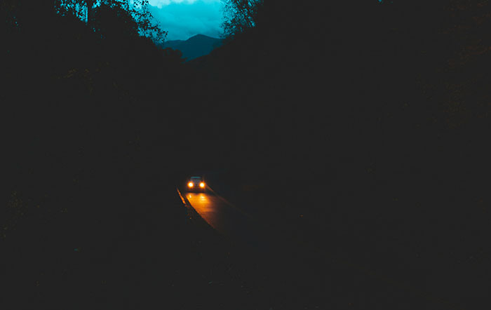Carretera oscura con un coche en movimiento, ilustrando personas que siguen vivas por decisiones espontáneas.