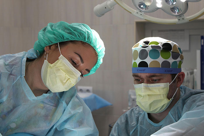 Dos médicos en cirugía, observando algo desconcertante sobre el cuerpo humano, con máscaras y gorros quirúrgicos.