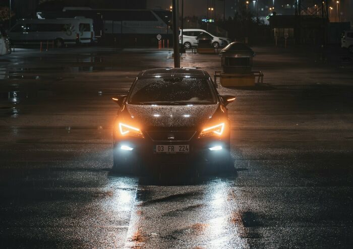 Coche con luces encendidas en un estacionamiento lluvioso de noche, simbolizando el momento de irse ya mismo.