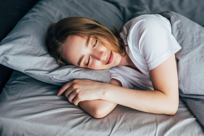 Mujer durmiendo plácidamente en cama con ropa blanca, imagen que refleja actividades aparentemente inofensivas con peligro.