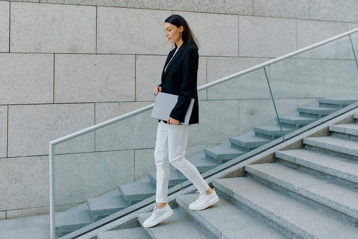 Mujer camina por escaleras urbanas con laptop, ilustrando actividades aparentemente inofensivas pero con riesgo oculto.