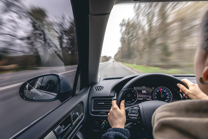 Persona conduciendo un automóvil a alta velocidad sobre carretera, mostrando riesgos de actividades aparentemente inofensivas.