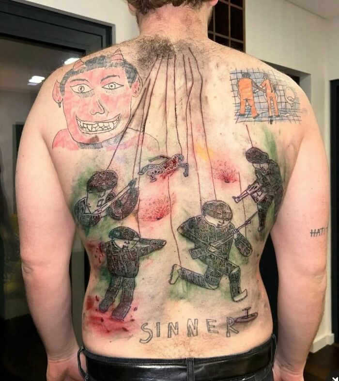 Horrible tatuaje en la espalda de una persona con figuras de soldados y un rostro rojo.