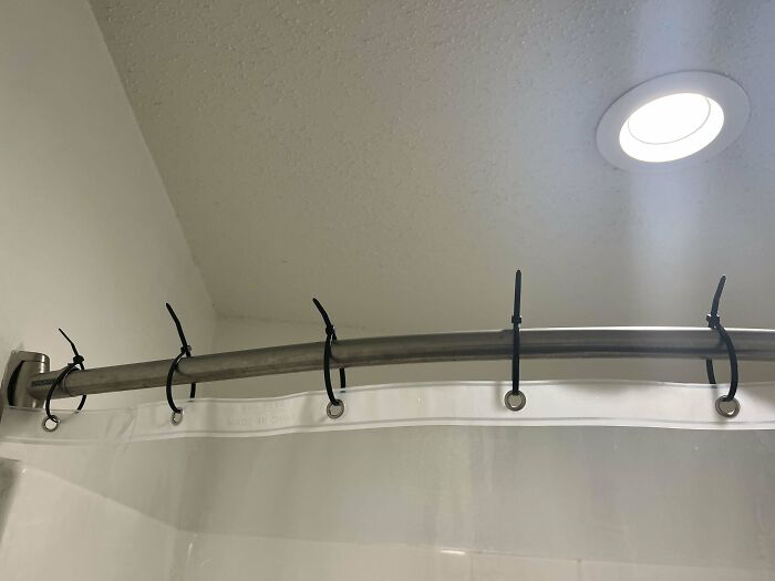 Cortina de ducha reparada con bridas, solución empeorando el problema inicial.