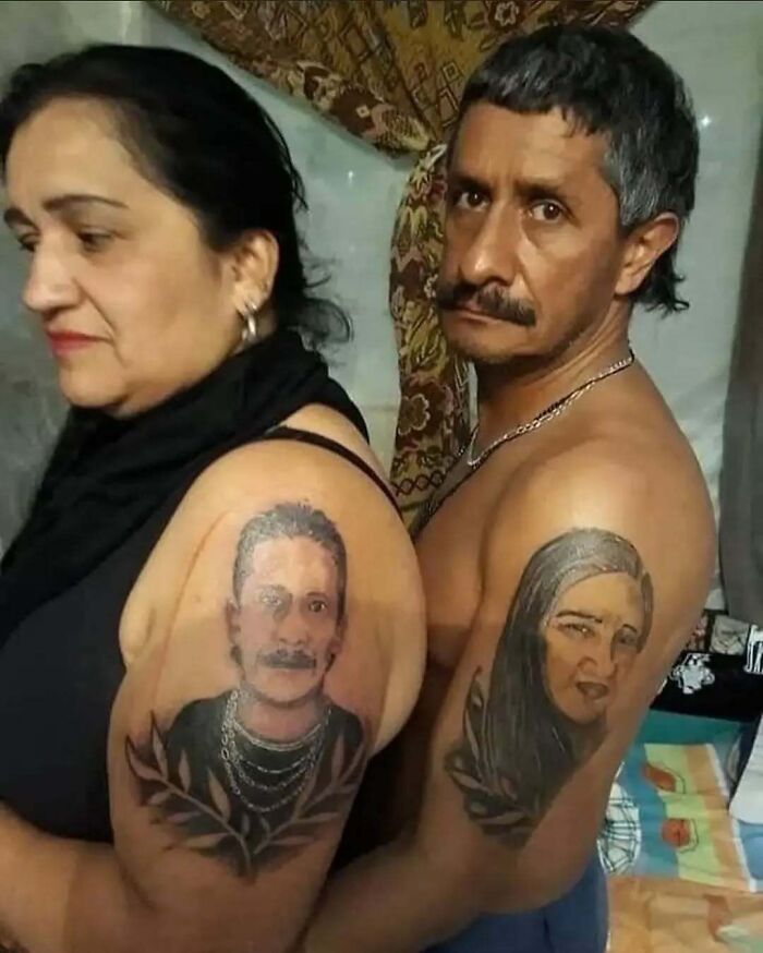 Dos personas mostrando tatuajes de rostros en sus brazos en una habitación decorada.
