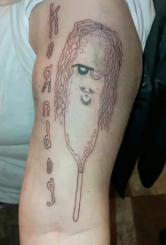 Un tatuaje mal hecho en el brazo con diseño confuso de un personaje con gafas.