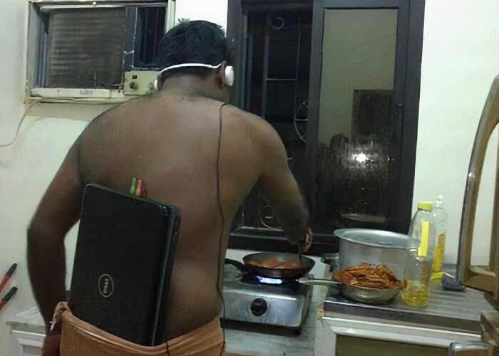 Hombre cocinando en casa con portátil atado a la espalda, escenario extraño y difícil de explicar.