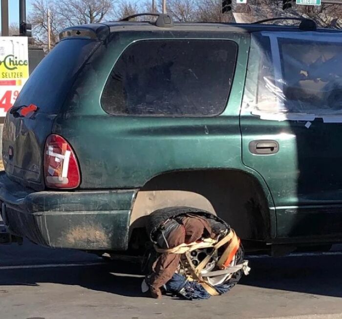 Auto con rueda trasera improvisada, mostrando un intento de reparación fallido en la calle.
