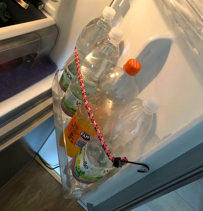 Estante de refrigerador con botellas aseguradas con una cuerda elástica; reparación que empeora el problema.
