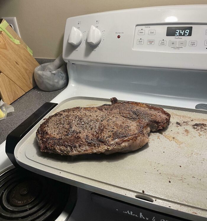 Bistec cocinado en una bandeja sobre la estufa con los controles visibles, humor de divertidos maridos.