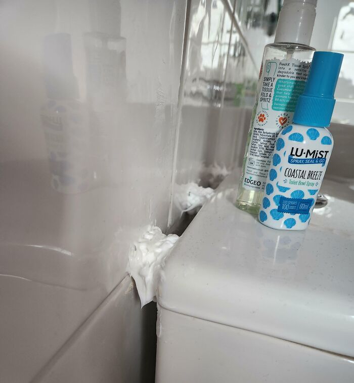 Espuma mal aplicada en el borde del lavabo con productos de baño, mostrando un intento fallido de reparación.