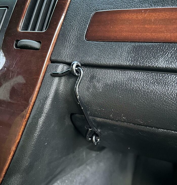 Intento fallido de reparar la guantera de un coche con un gancho metálico improvisado.