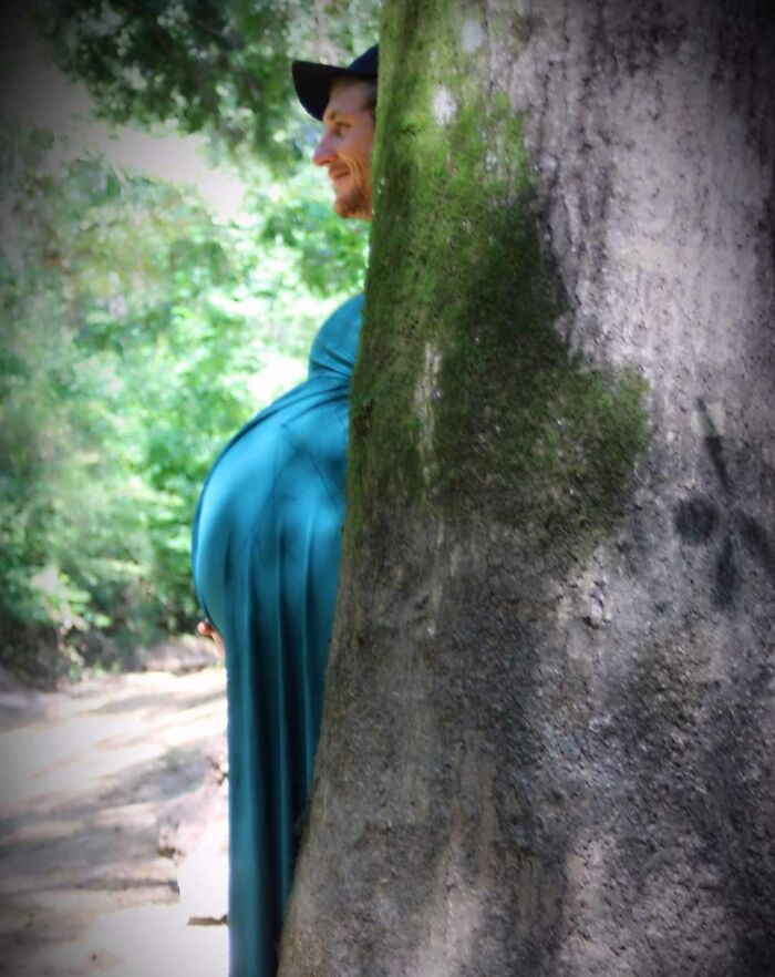 Un divertido marido se esconde detrás de un árbol con un efecto cómico en su barriga.
