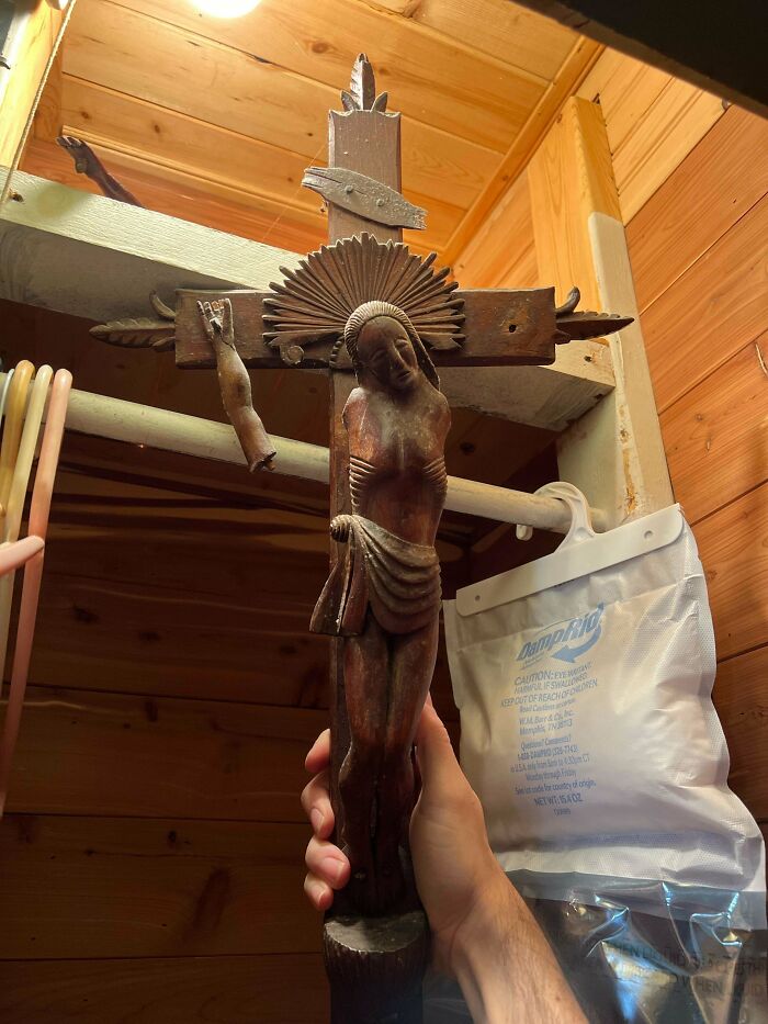 Escultura de Cristo crucificado antiguo con brazo roto sostenida en una casa de madera tras mudanza sorpresa.